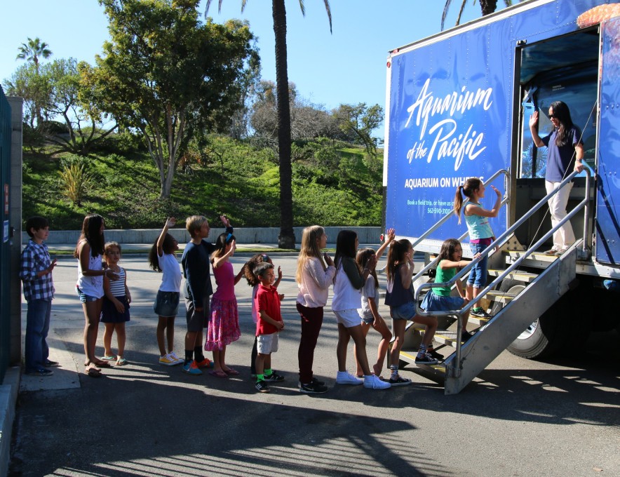 About a dozen children form a line outside the Aquarium on Wheels box truck while an educator welcomes them in from the top of the stairs.