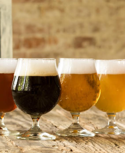 Four round glasses of various colored beer with a rich head of foam on top.