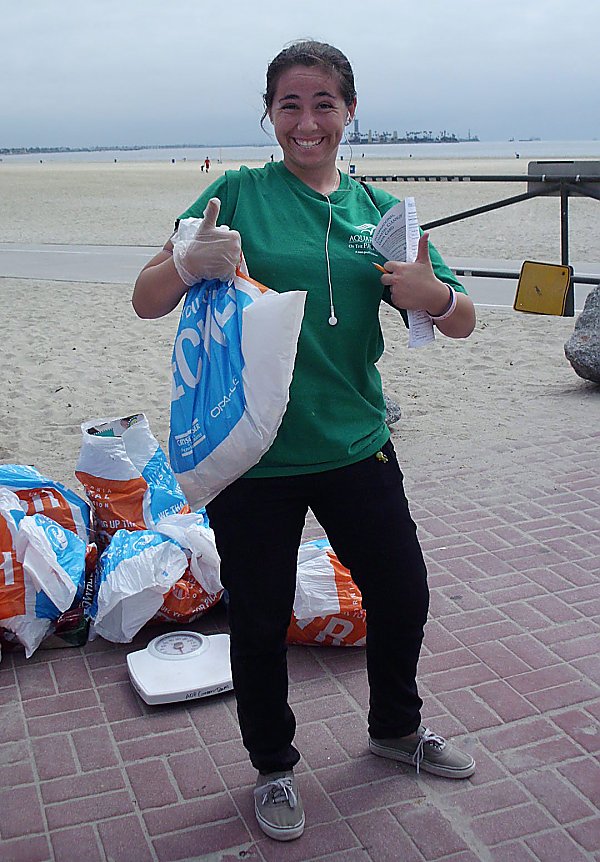 Young woman holds thumbs up with a trash bag at a beach cleanup
