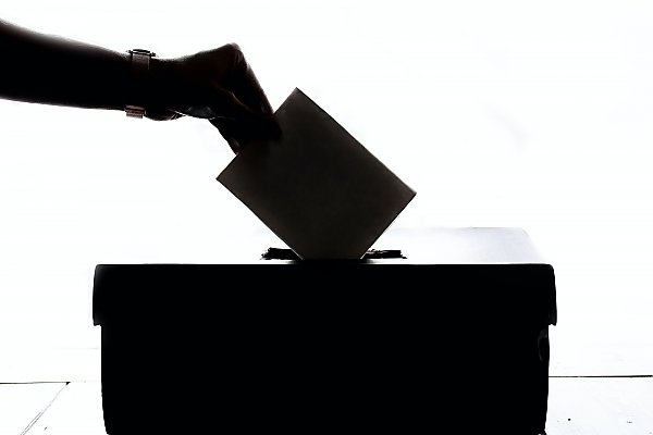 silhouette of a hand submits a ballot in a box