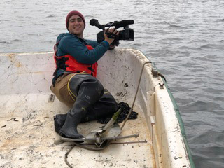 Camera operator Bailey Galvin-Scott is dressed in wadders on a boat, ready to get some images from the Hog Island Oyster Farm.