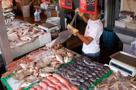 Man pours ice over fish on display at a seafood market.