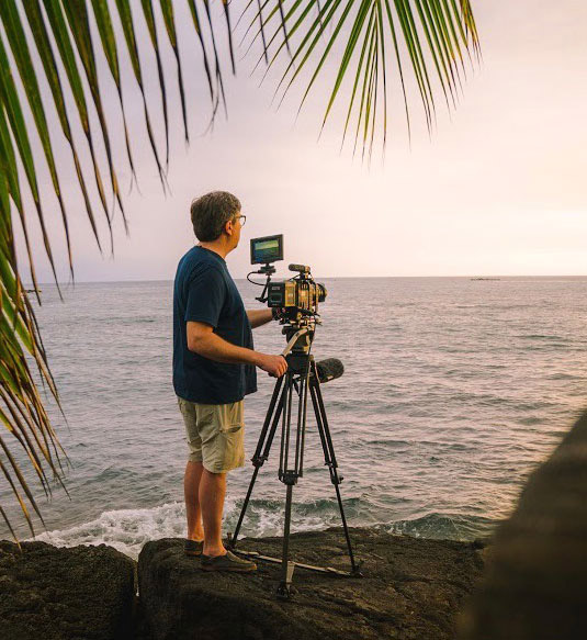 Andrew Cohen films Hawaii sunset with palm fronds in foreground.