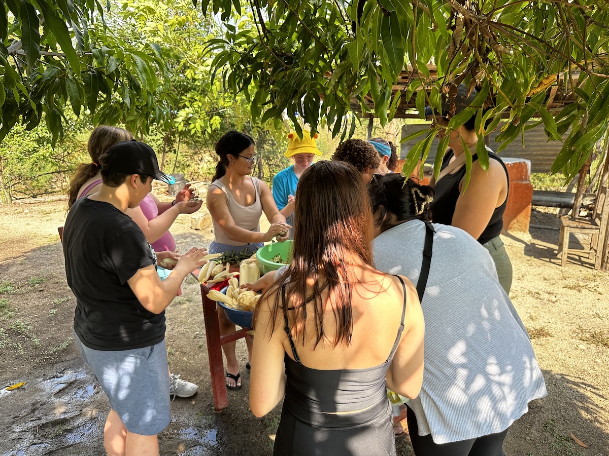Students gathered around a table outside to make tamales