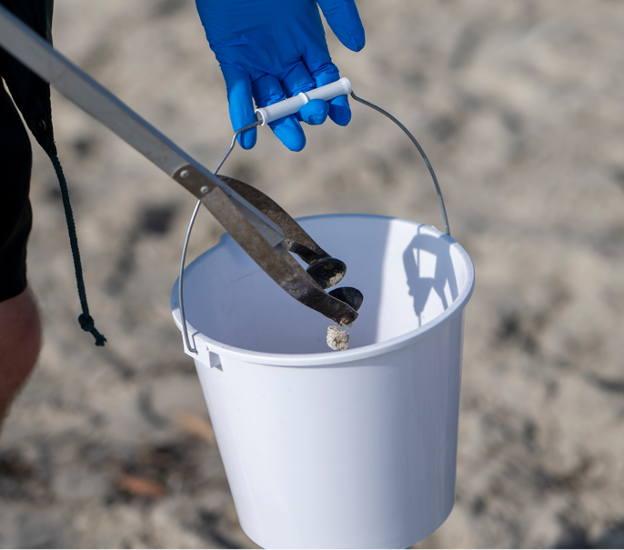 A volunteer adds marine debris into their bucket at an Aquarium cleanup.