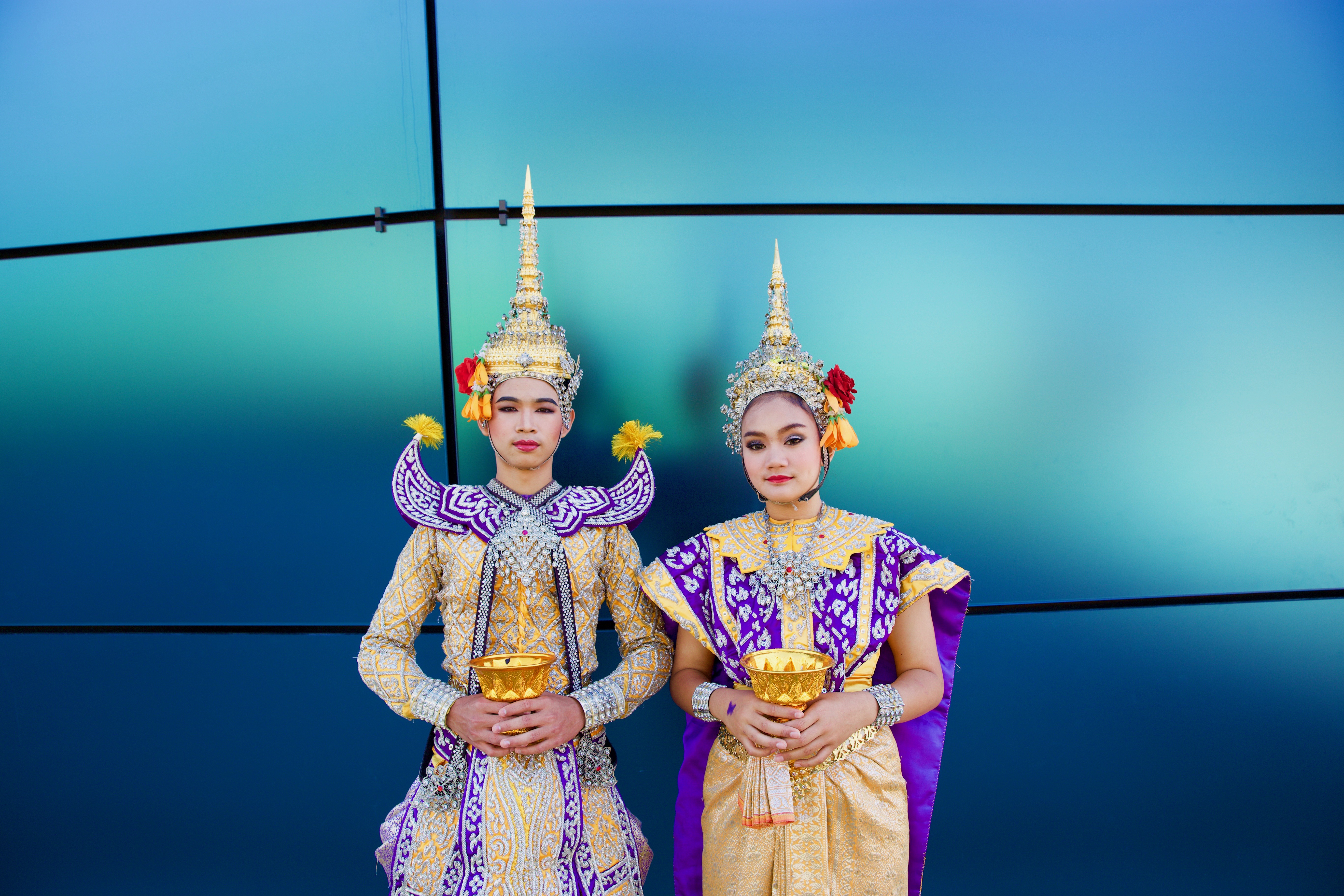 two people dressed in southeast asian ornate dress with a blue background