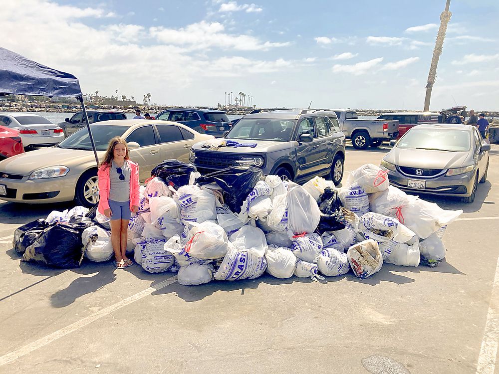 Child standing next to a pile of filled trash bags from the Coastal Clean-up
                      event