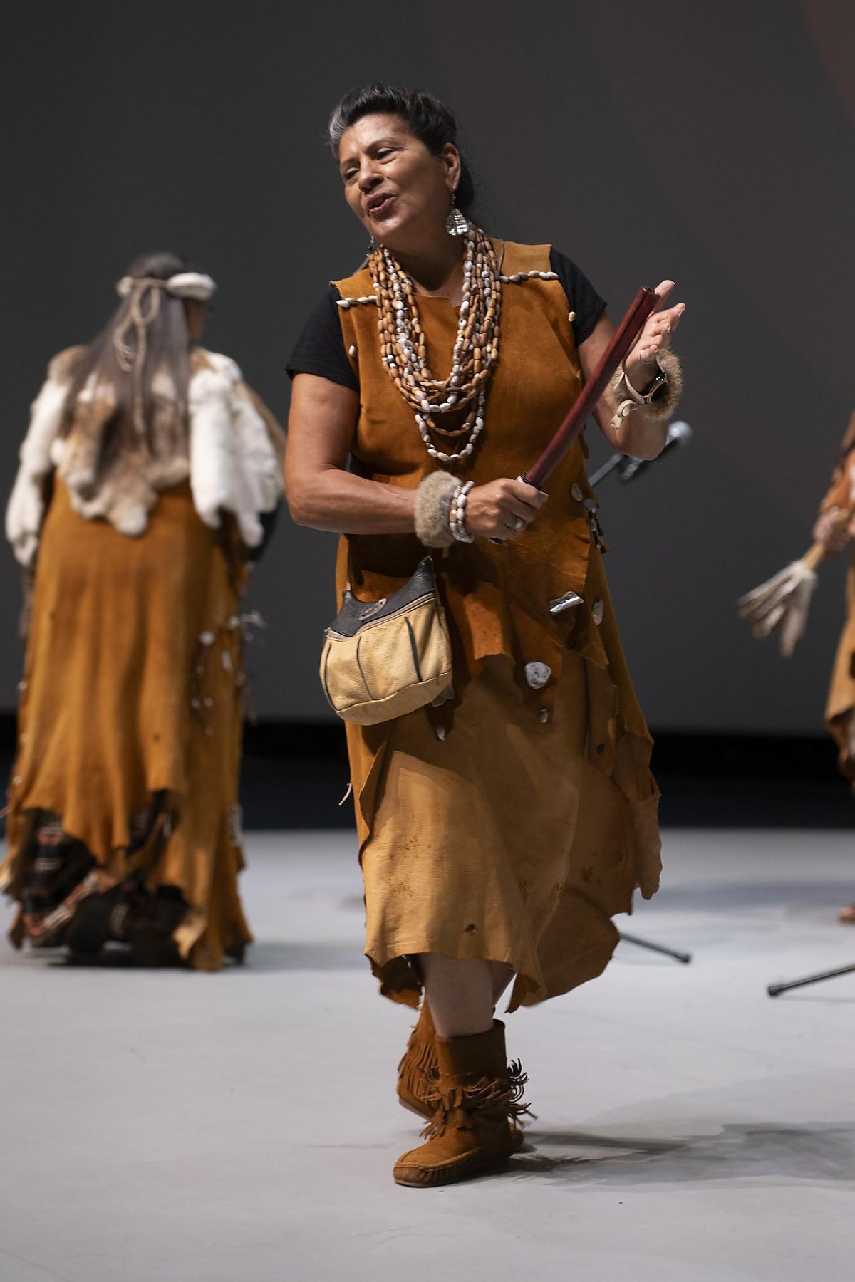 Chumash Family Singers/Storytellers hitting a stick on her open palm on a stage