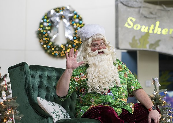 Santa with white hair and beard waves hello
