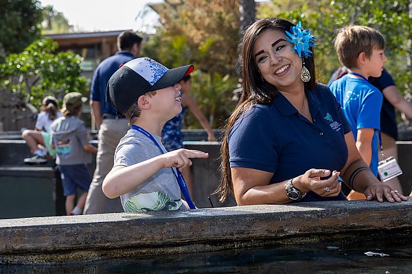 Boy shows two-finger-touch hand in Shark Lagoon accompanied by an Aquarium educator