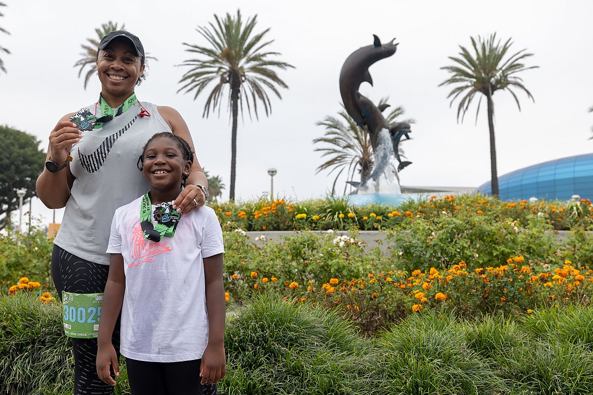 woman and girl pose with their running medals in front of dolphin fountain