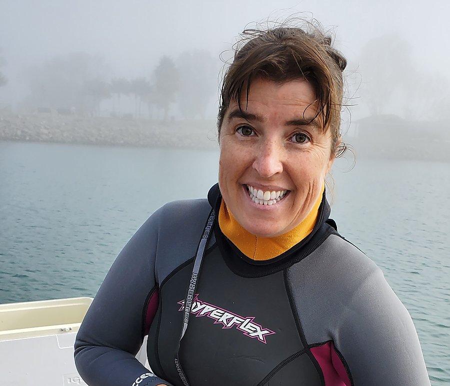 A smiling Nancy Caruso wears a wetsuit on a boat on the water