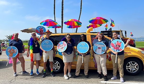 Aquarium volunteers pose with the yellow sub minivan during a pride parade holding Pacific Pals signs.