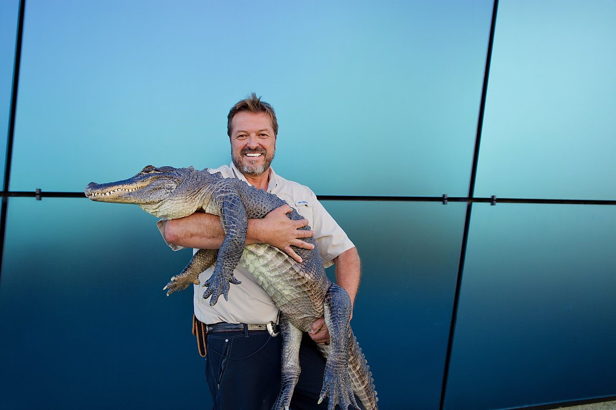 A man smiles while holding an alligator in his arms