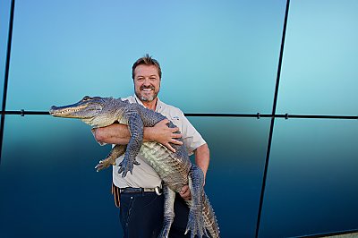 A man smiles while holding an alligator in his arms