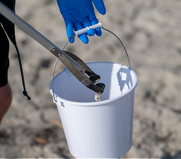 A volunteer adds marine debris into their bucket at an Aquarium cleanup.