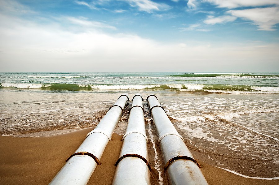 Three large pipes point towards beach with crashing waves