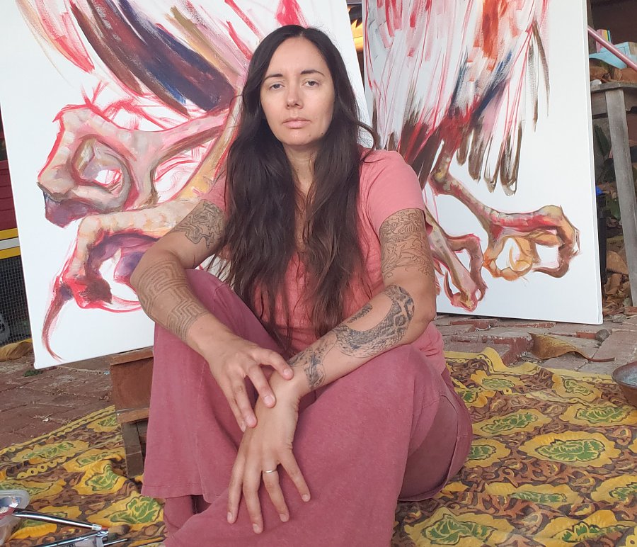 woman with long hair sitting down in front of a large painting