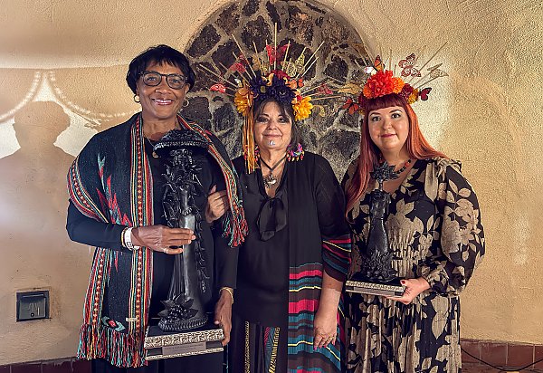 Three people standing should to shoulder; two of the people are holding awards.
