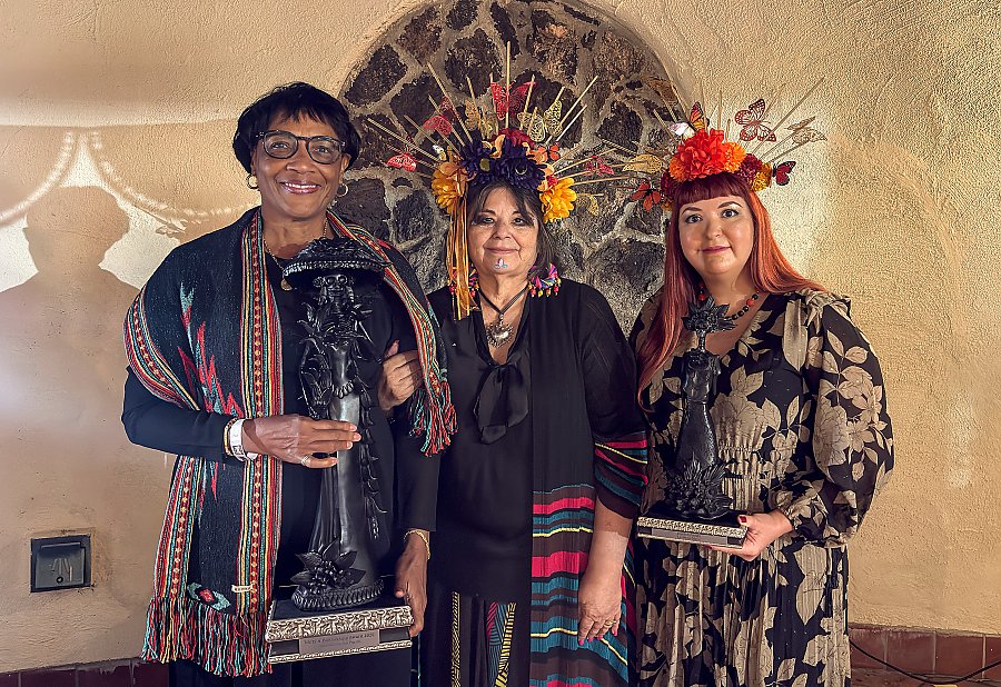 Three people standing should to shoulder; two of the people are holding awards.