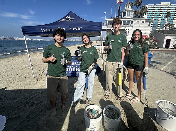 Four people in green shirts standing on a beach and parking lot while holding grabbers
