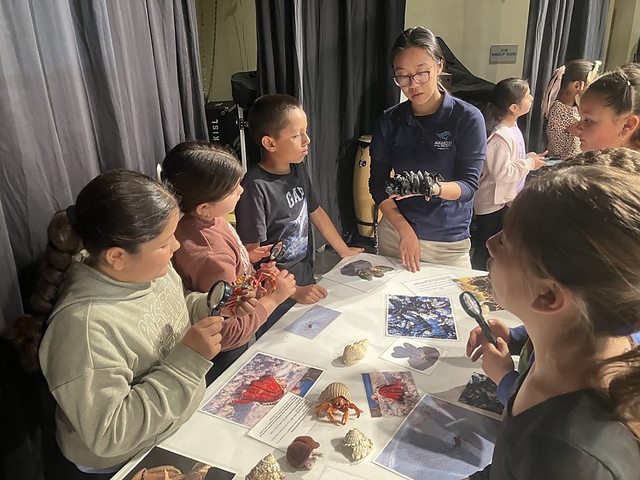 an educator holds a model for young students while they all stand at a table