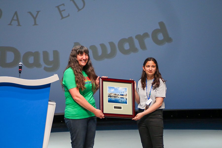 Two women holding framed award next to podium