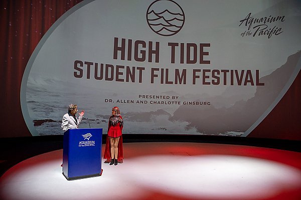 Dr. Allen & Charlotte Ginsburg present on stage at the High Tide Student Film Festival with screen projecting said name of event behind them