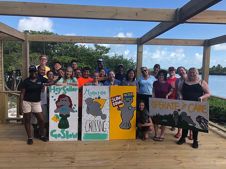 Students pose on doc with manatee signs