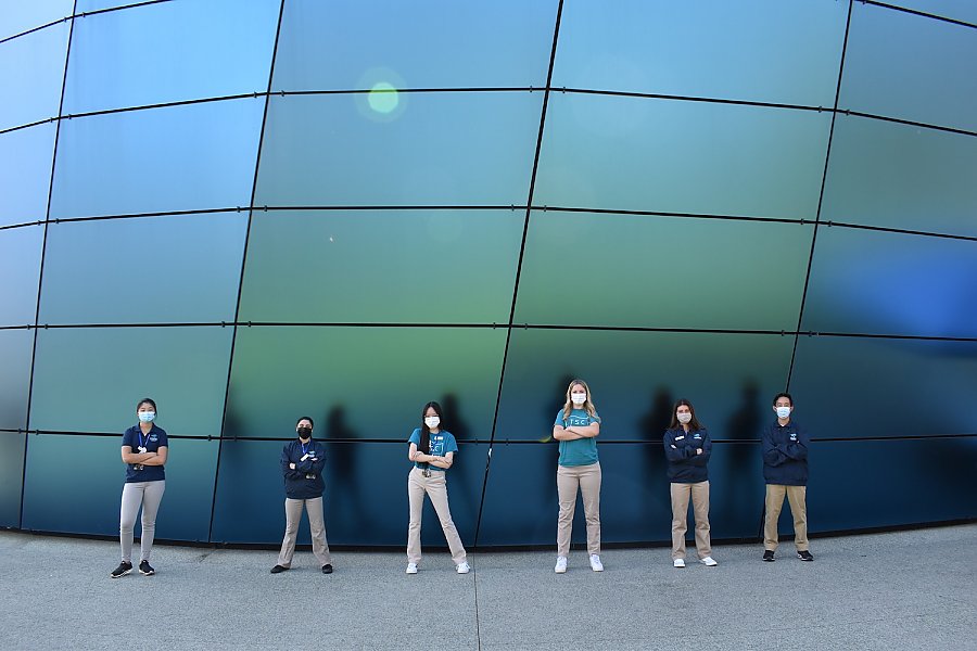 Six Teen Science Cafe Volunteers pose confidently in front of Pacific Visions blue glass wall