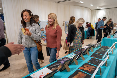 Women smile and laugh next to tables with silent auction items.